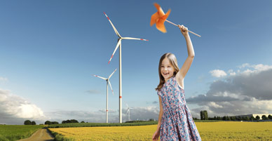 Mädchen auf Feld mit Energiewindräder hält Spielzeugwindrad in der Hand